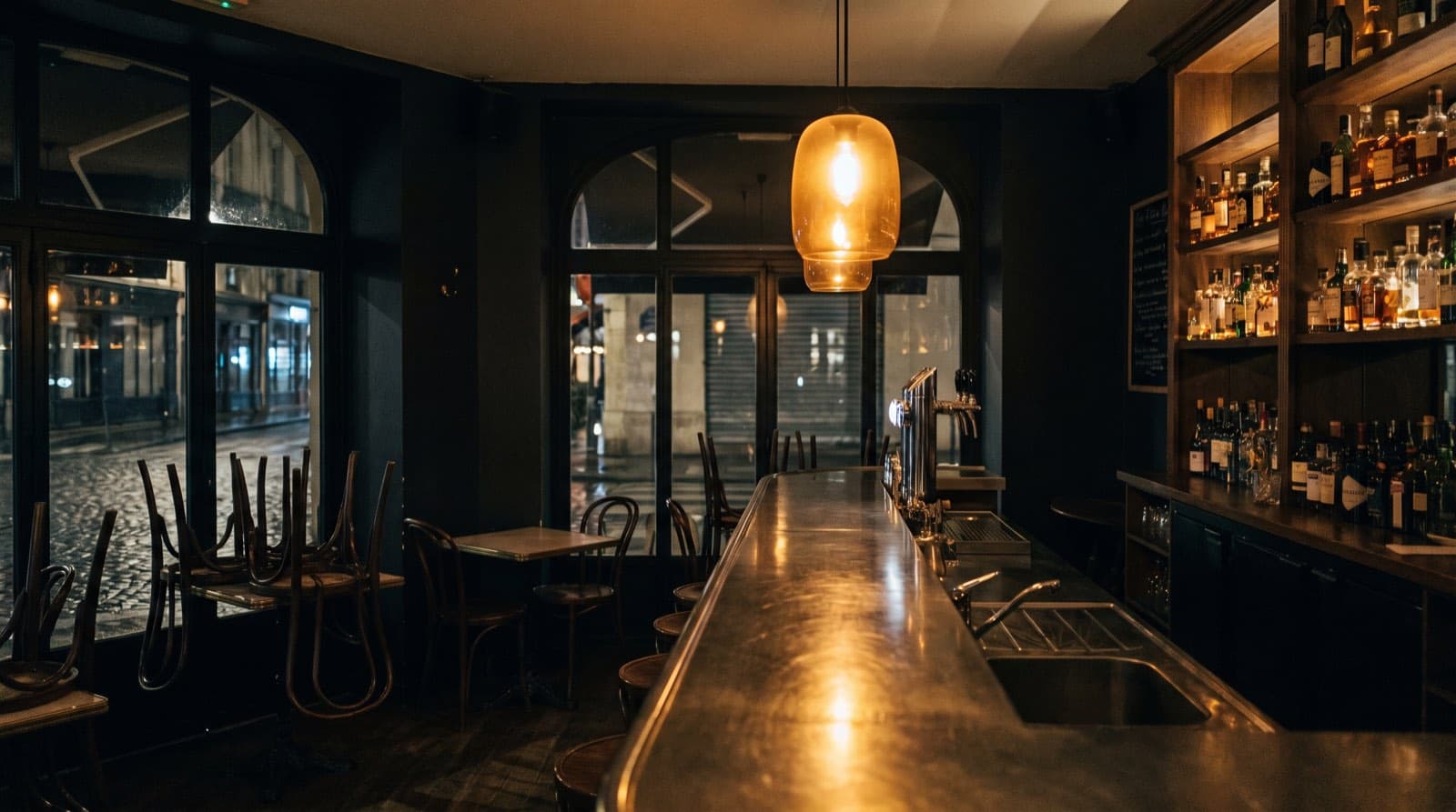 Salle de bistro parisien de nuit, comptoir en zinc sous une lampe ambre