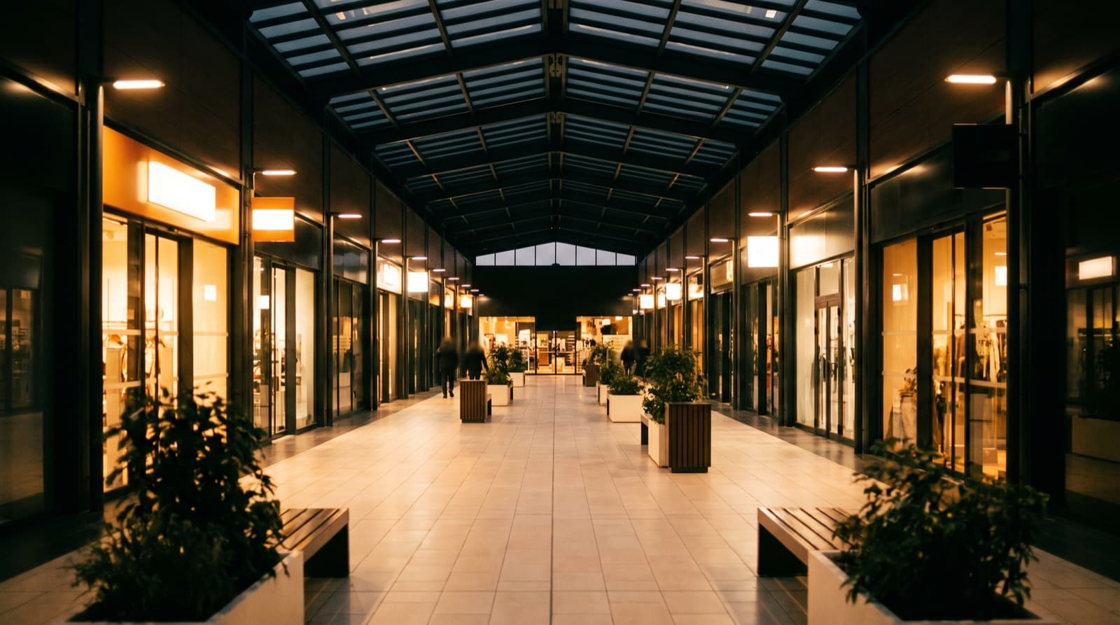Galerie marchande d'un centre commercial en fin de journée, vitrines éclairées et bancs