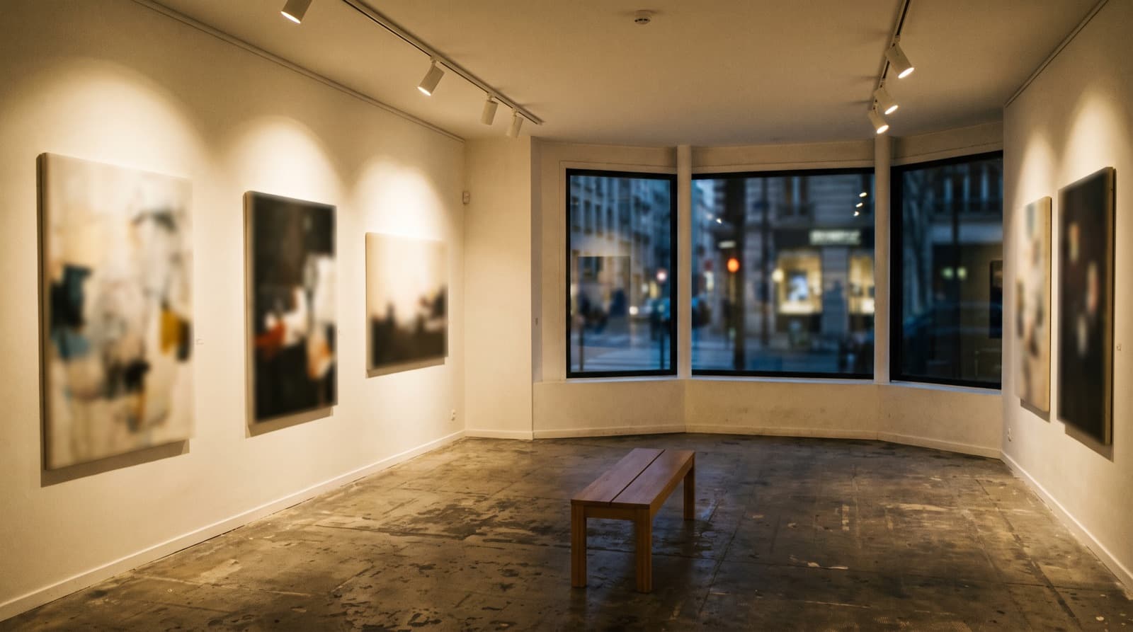 Salle d'exposition d'un lieu culturel le soir, murs clairs et spots muséaux