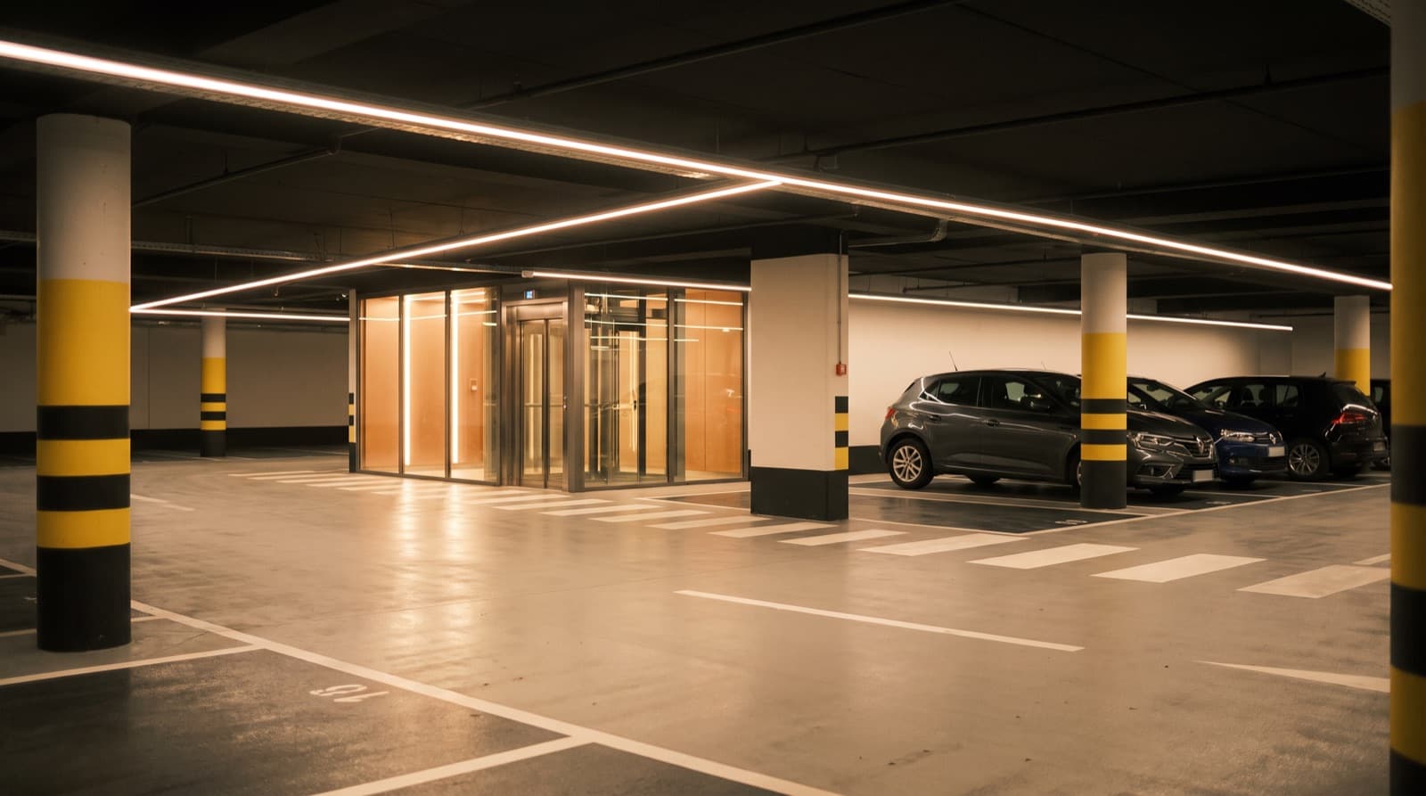 Parking couvert récent la nuit, lignes LED au plafond et sas vitré d'ascenseur